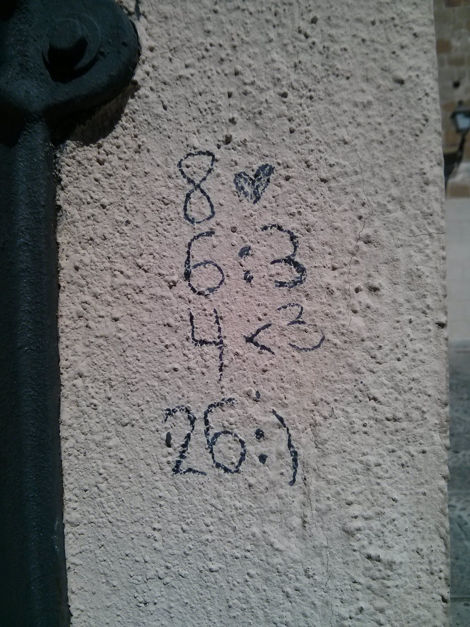 Sobre una pared rugosa de cemento blanco, pintado con rotulador aparecen: 8 corazón, salto de línea, 6:3, salto de línea, 4<3, salto de línea, 26:)