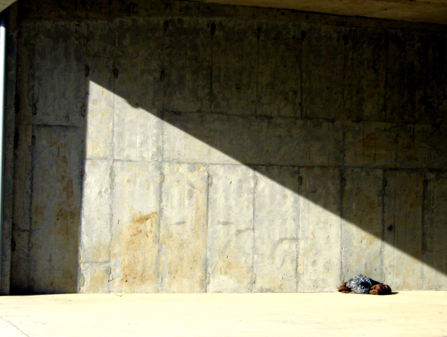 Rodeado por sombras, la luz dibuja un triángulo rectángulo sobre una pared. En el límite entre el suelo y la pared, cerca del ángulo agudo, hay un montón de ropa.